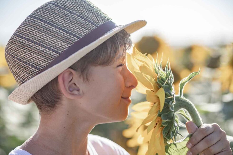 Primer plano del perfil de un niño con sombrero en un campo de girasoles