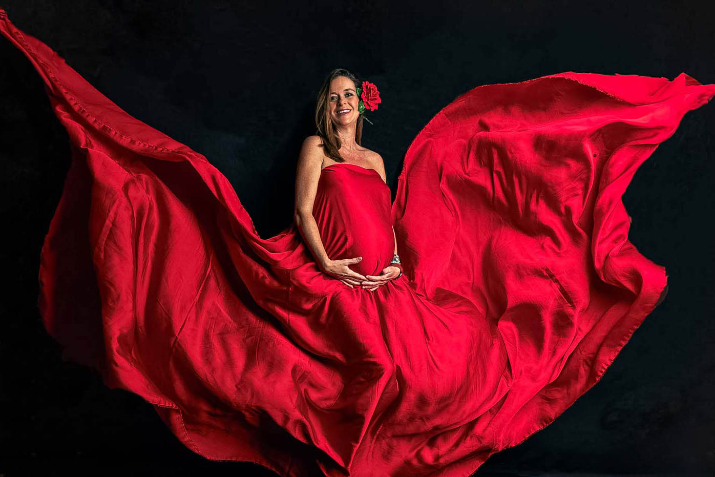 Mujer embarazada sonriente con una tela roja que la envuelve y marca la silueta