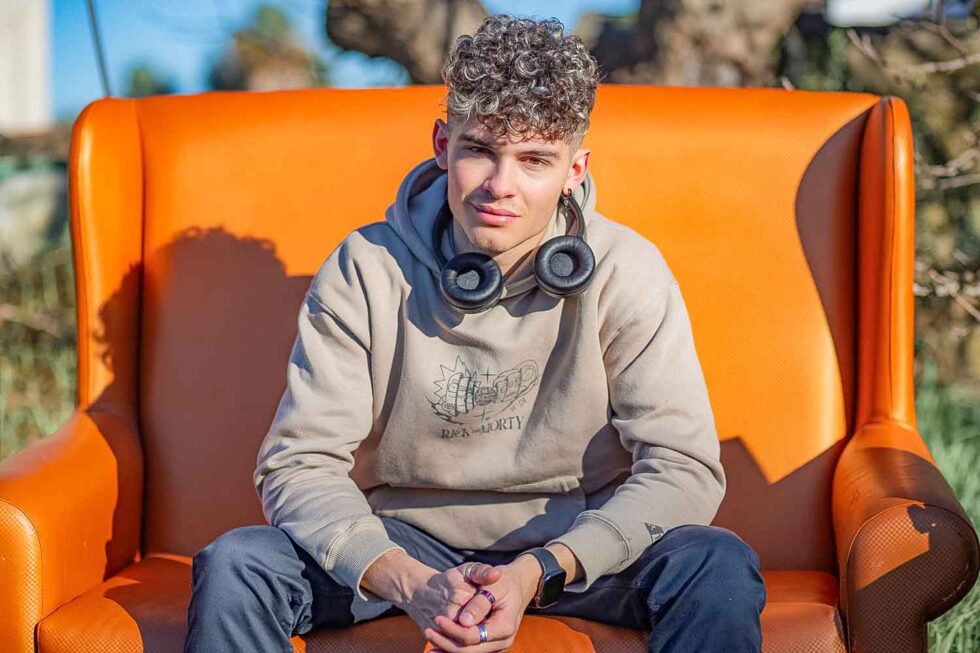 Fotografía de retrato de un joven de estilo urbano con auriculares mirando a cámara y sentado en un sofá en un campo
