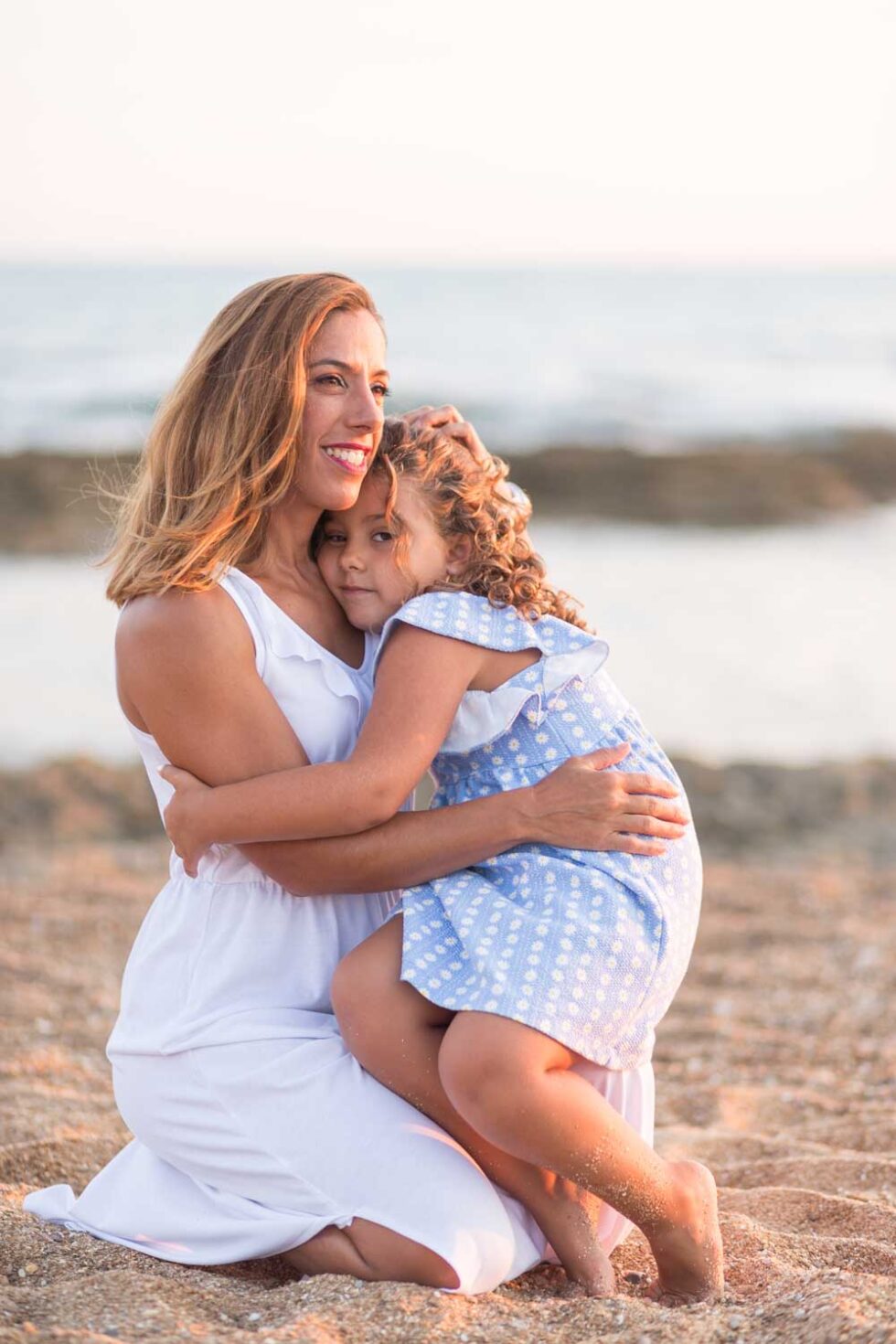 Madre arrodillada con su hija pequeña agarrada en una playa de Chiclana