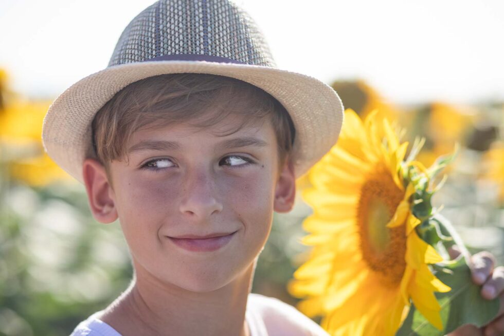 Primer plano de chico con sombrero junto con un girasol en un campo