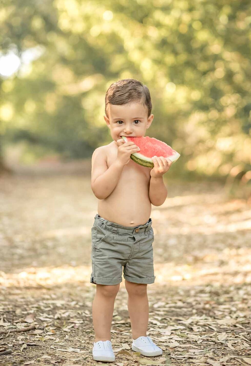 Bebé de pie mordiendo una rodaja de sandía en un ambiente natural