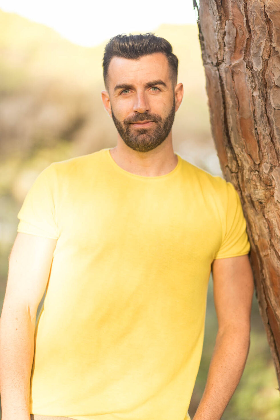 Hombre apoyado en un árbol mirando a cámara en en un ambiente natural