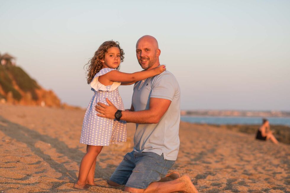 Un padre abraza a su hija pequeña al atardecer en una bonita playa durante la sesión de fotografía de familias