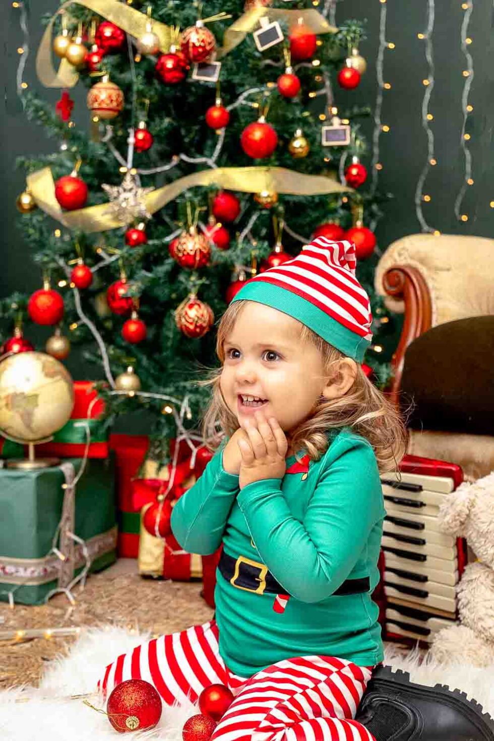 Niña disfrazada de elfo navideño muy sonriente con un bonito fondo con árbol de Navidad, regalos y luces