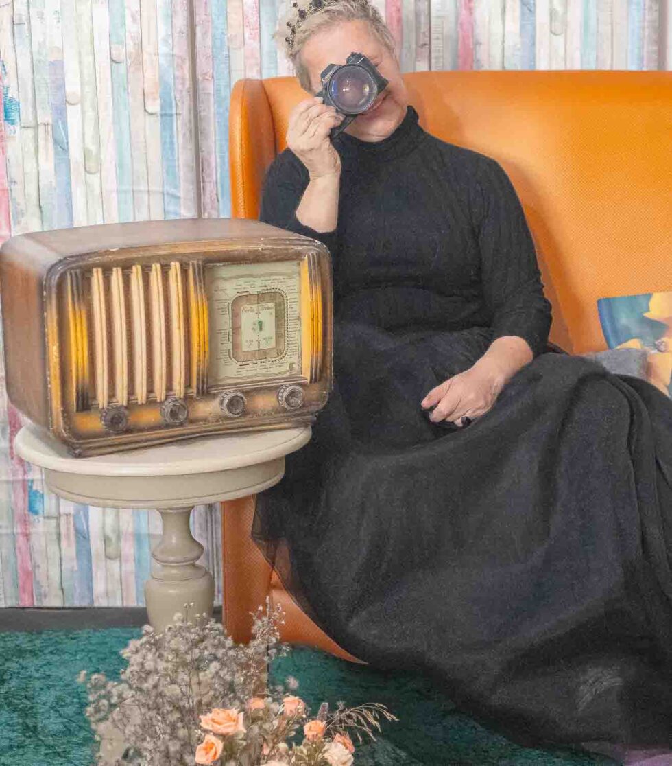 Mujer sentada en un sofá junto a una radio antigua con una cámara en la mano