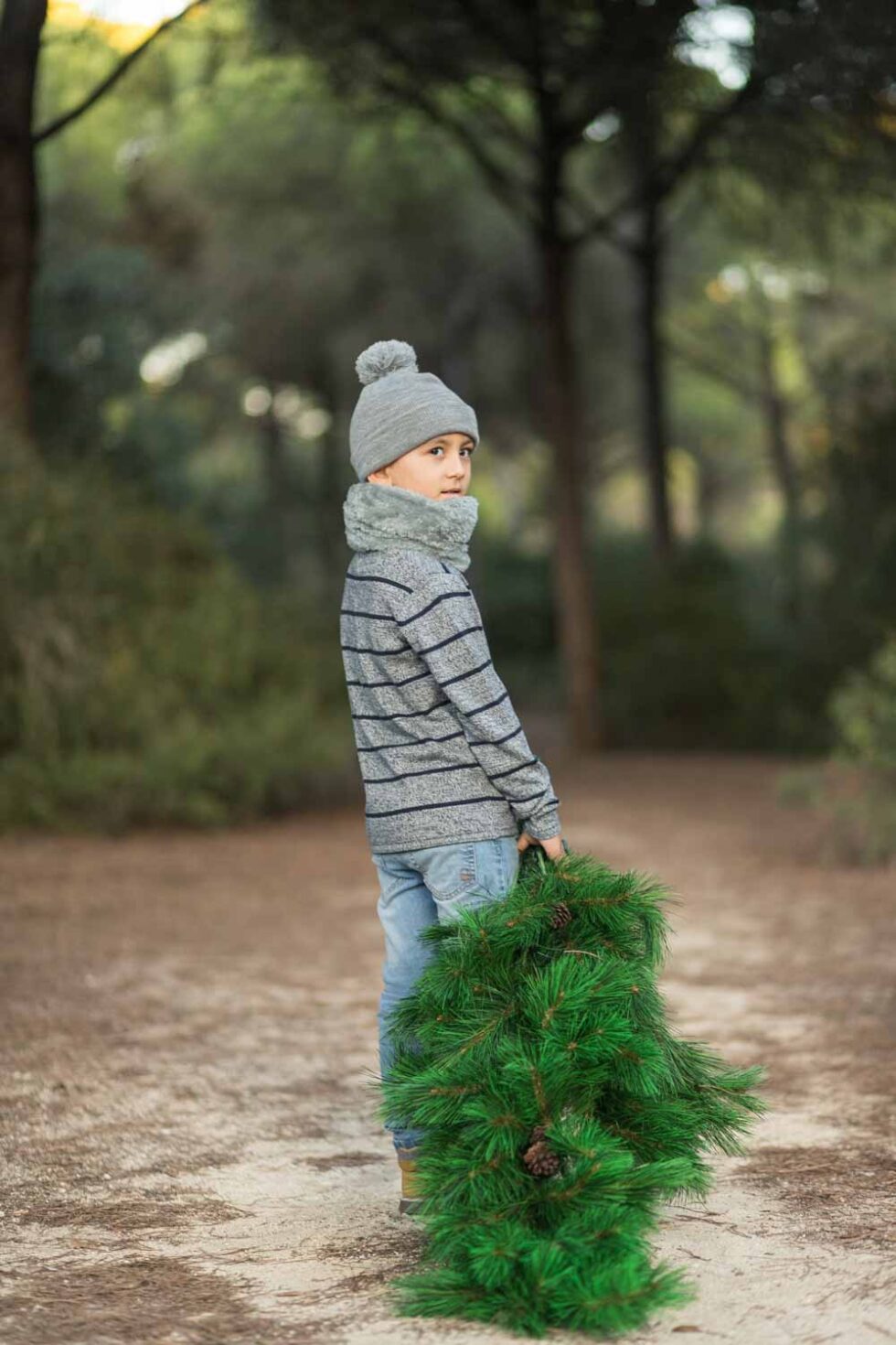 Chico vestido con ropa de invierno sosteniendo un árbol de Navidad en un bosque