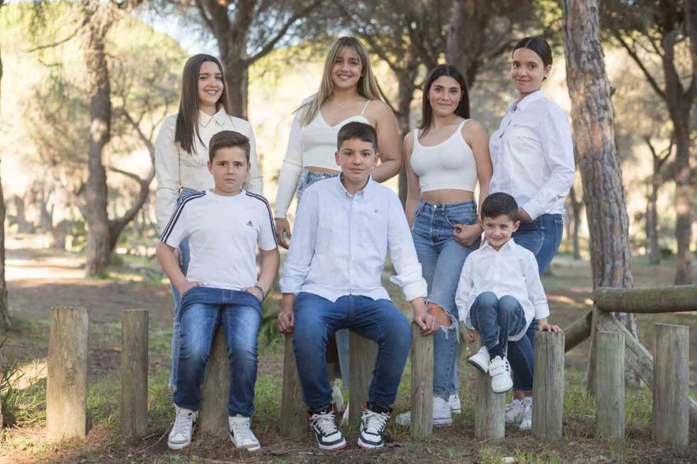 Cuatro niñas y tres niños vestidos con vaqueros y camisa blanca posan sonrientes mirando a cámara en un parque en Chiclana