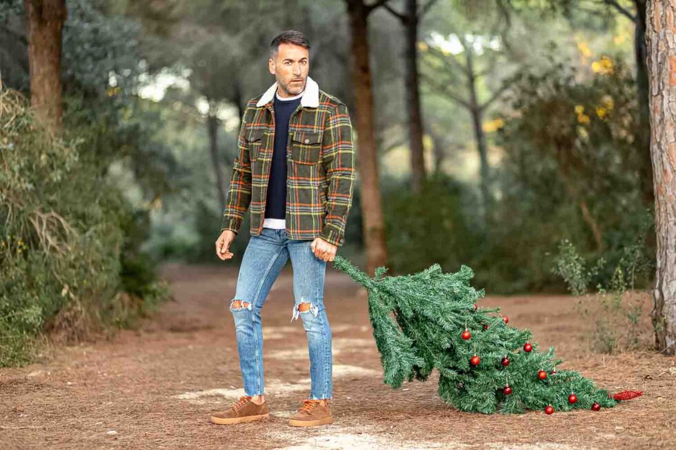 Hombre con ropa de abrigo arrastrando un árbol de Navidad por el bosque