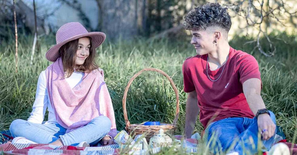 Chico y chica mirándose sonrientes en una sesión de fotos simulando un picnic