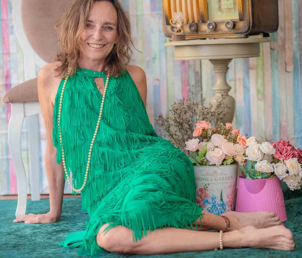 Mujer sonriente con vestido de flecos y collar de perlas posando en un decorado vintage