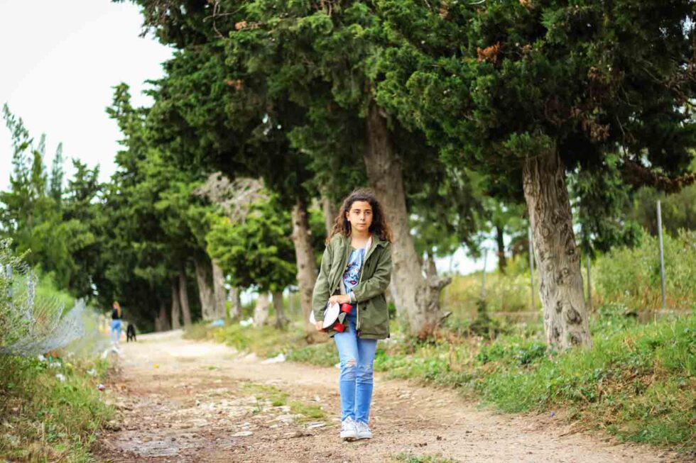 Niña caminando por un camino natural con su monopatín bajo el brazo