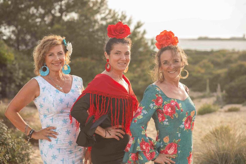 Tres mujeres vestidas de flamenca mirando a cámara sonrientes en un entorno natural