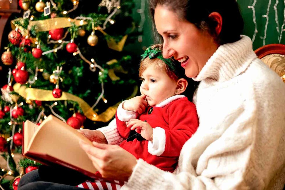 Plano corto de madre son su bebé mirando un libro en un ambiente muy navideño