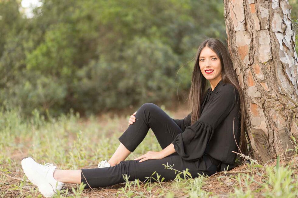 Mujer sentada y apoyada en un árbol mirando a cámara y sonriendo