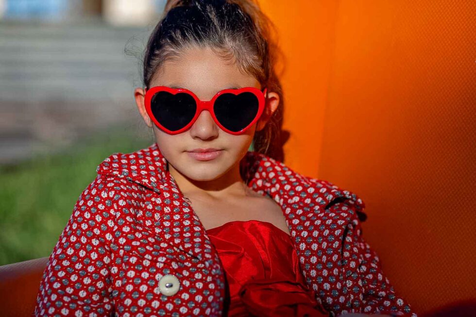 Primer plano de niña con gafas de sol con forma de corazón mirando a cámara en una sesión de fotos en exteriores