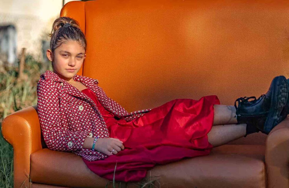 Chica joven tumbada de lado en un sofá mirando a cámara